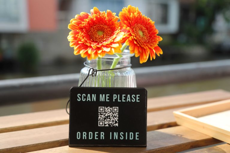 17.06.2023, Erfurt, in einem Cafe steht ein Schild an einer Blumenvase mit frischen Gerbera (Blumen) - Scan me please Order inside - ueber einen QR-Code kann man die Speisekarte abrufen Foto: Karina Hessland-Wissel